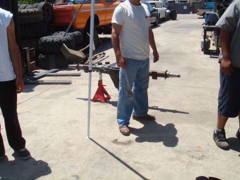 1992 Ford Bronco - An axle assembly is supported by jack stands, with a partial view of an orange truck and stacked tires.