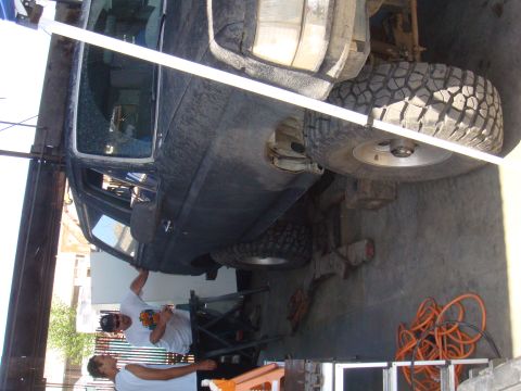 1992 Ford Bronco - Two men work on a dark SUV lifted for service. The specific year and model are not identifiable from this angle.
