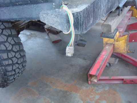 1992 Ford Bronco - The rear of a vehicle is shown, supported by jack stands, with a wiring harness dangling near the frame.