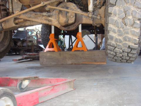 1992 Ford Bronco - Undercarriage of a vehicle being supported by jack stands and wooden blocks in a workshop.