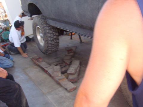 1992 Ford Bronco - Mechanics work on the suspension of a gray 1992 Ford Bronco, with leaf springs laid out on the floor.