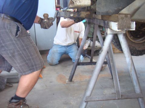 1992 Ford Bronco - Men work on the axle assembly of a vehicle supported by jack stands.