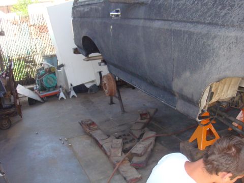 1992 Ford Bronco - A Ford Bronco is raised on jack stands in a garage, with a person working on it. The vehicle appears to be undergoing maintenance.