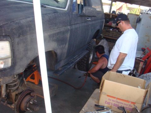 1992 Ford Bronco - Mechanics work on a dark 1992 Ford Bronco, which is raised on jack stands for maintenance.