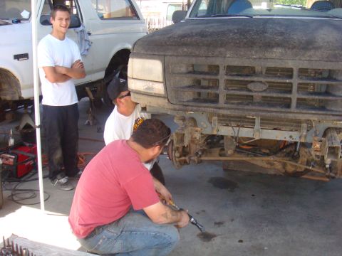 1992 Ford Bronco - Mechanics work on the front end of a 1992 Ford Bronco, with the grille and bumper removed.