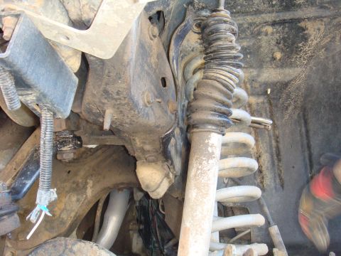 1992 Ford Bronco - Close-up view of the front suspension system, showing a shock absorber with a protective rubber boot and a coil spring.