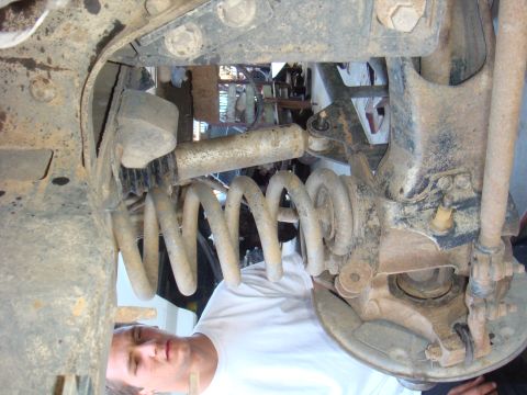 1992 Ford Bronco - Close-up of a vehicle's rear suspension, showing the coil spring and shock absorber. A person is inspecting the parts.
