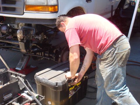 1992 Ford Bronco - Mechanic works on the front suspension of a white truck, with tools nearby.