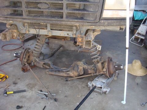 1992 Ford Bronco - The front axle and suspension system are disassembled, with parts laid out on the floor.