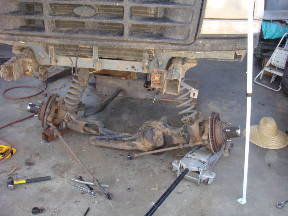 Front axle and suspension parts removed from a vehicle, with tools on the ground