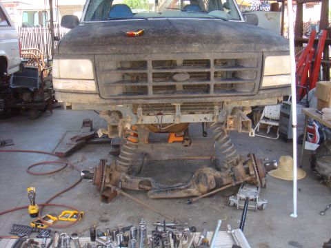 1992 Ford Bronco - The front axle and suspension of a 1992 Ford Bronco are removed, revealing the underside of the truck and a collection of tools.