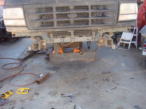1992 Ford Bronco - The front end of a vehicle is disassembled and supported by jack stands in a workshop setting.