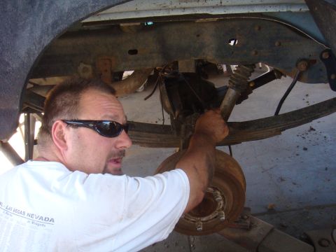 1992 Ford Bronco - Man in sunglasses works on the rear suspension of a 1992 Ford Bronco, focusing on the axle and shock absorber.