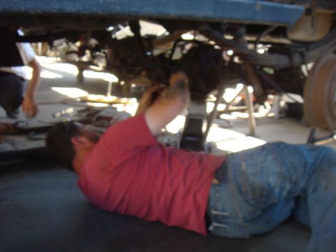 1992 Ford Bronco - A mechanic works on the undercarriage of a vehicle that is raised on jack stands.