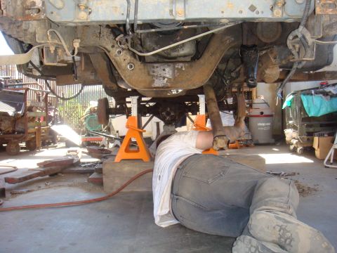 1992 Ford Bronco - Mechanic works on the undercarriage of a vehicle supported by jack stands in a garage.