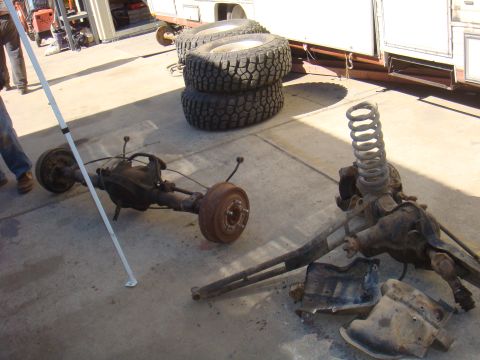 1992 Ford Bronco - Disassembled vehicle axles and tires are laid out on a concrete surface with a camper in the background.