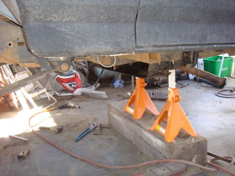 1992 Ford Bronco - The underside of a vehicle is supported by jack stands in a workshop setting, with various tools scattered around.