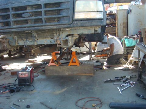 1992 Ford Bronco - Front end of a 1992 Ford Bronco is elevated on jack stands as a mechanic works on the undercarriage.