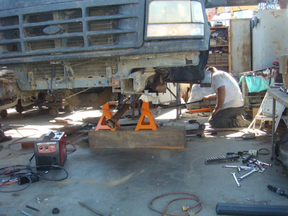 1992 Ford Bronco front end on jack stands with mechanic working underneath