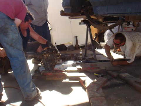 1992 Ford Bronco - Several individuals are gathered around a vehicle's undercarriage, focusing on the rear axle assembly during a repair or modification.