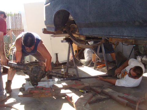 1992 Ford Bronco - Mechanics are seen working on the rear axle of a vehicle that is elevated on jack stands.
