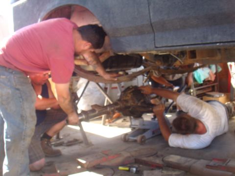 1992 Ford Bronco - Several people are gathered to work on the undercarriage of a vehicle, focusing on the rear axle assembly.