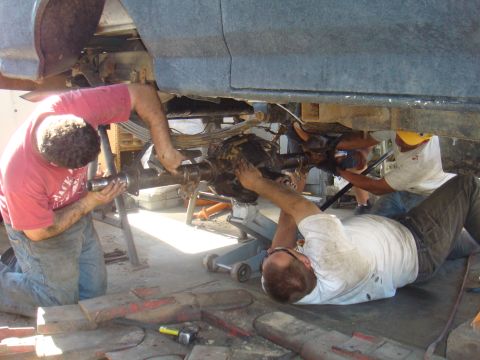 1992 Ford Bronco - Several individuals are actively engaged in servicing the rear axle of a vehicle, with tools and parts scattered around the work area.