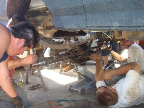 1992 Ford Bronco - Several individuals are actively engaged in servicing the rear axle of a vehicle, suggesting maintenance or repair work.