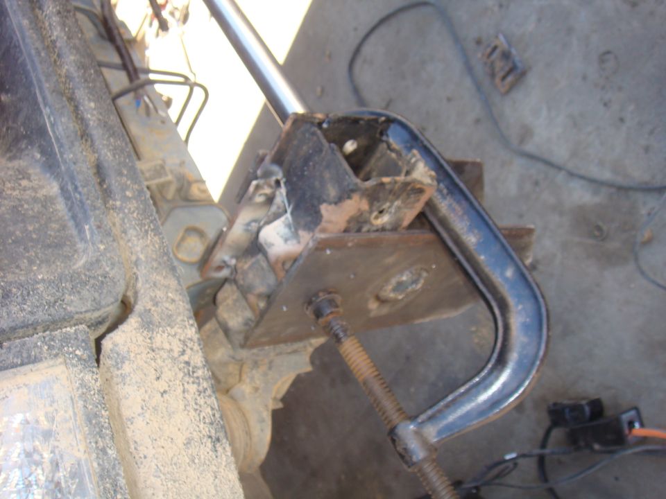 Close-up of a C-clamp holding a rusty metal bracket on a vehicle's suspension component