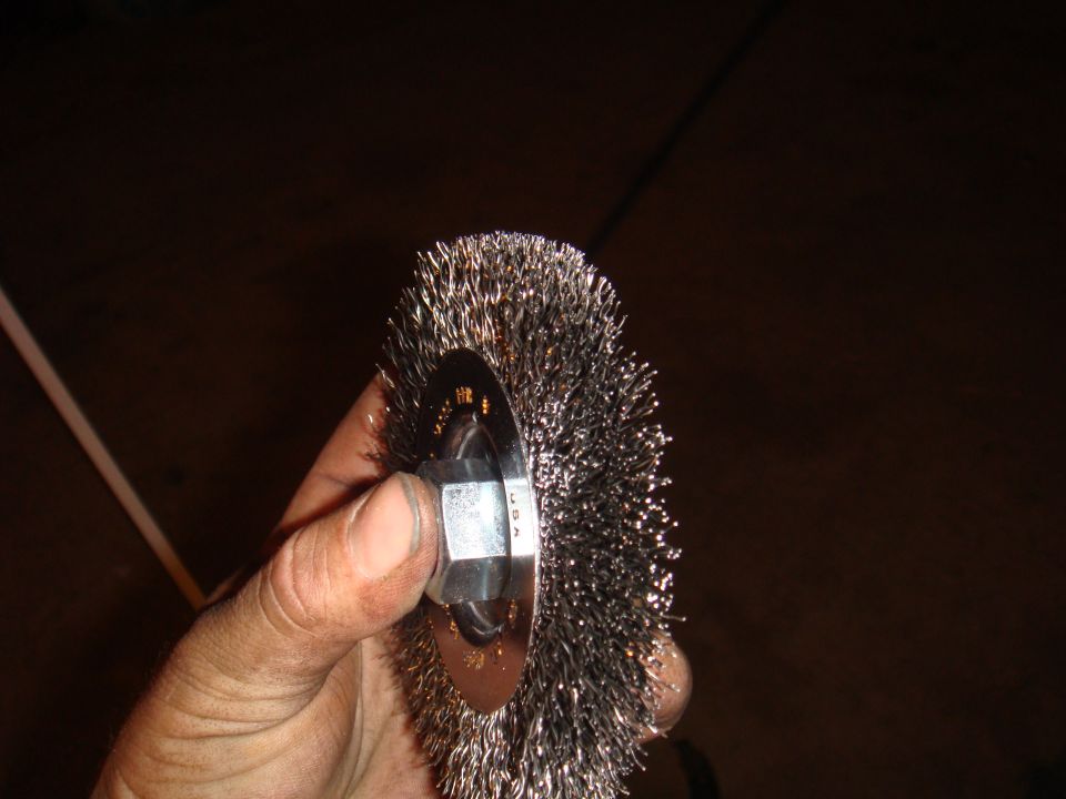 Hand holding a wire wheel brush with a hex nut attachment. Text on brush reads 'USA'