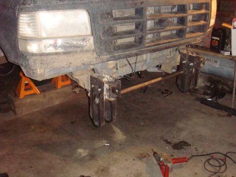 1992 Ford Bronco - The front of a truck is elevated on jack stands, revealing modifications to the bumper and frame.