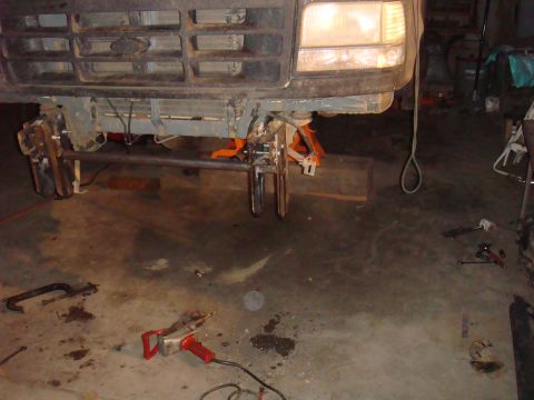 1992 Ford Bronco - The front axle of a 1992 Ford Bronco is suspended on jack stands in a garage, with tools scattered around.