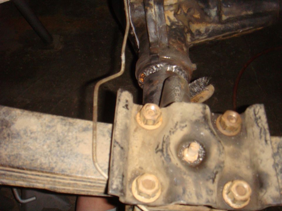 Close-up of a welded rear axle with leaf spring mounts and bolts. A wire runs nearby
