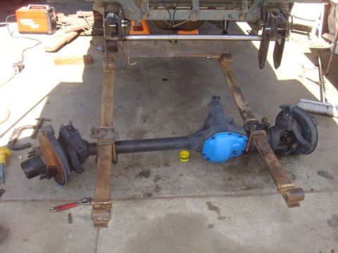 1992 Ford Bronco - Front axle assembly, likely from a truck or SUV, is shown with its leaf springs detached and resting on the ground.