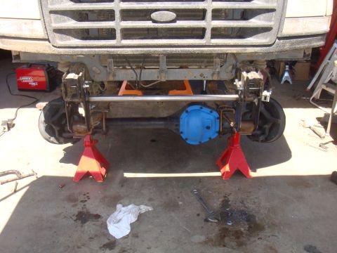 1992 Ford Bronco - Front axle assembly of a truck, supported by jack stands, with a blue differential cover. A Lincoln welder is present in the scene.