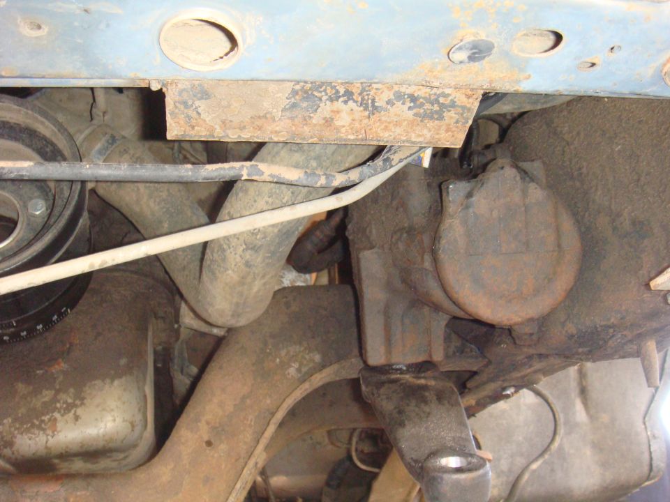Underside of a vehicle showing suspension components, engine parts, and exhaust pipes. Some rust is visible