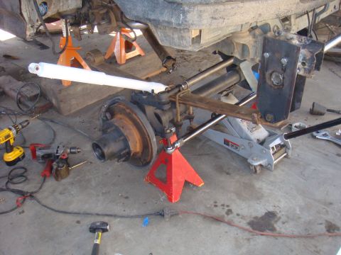 1992 Ford Bronco - The vehicle's axle assembly is supported by jack stands and a hydraulic jack, with various tools scattered around the work area.