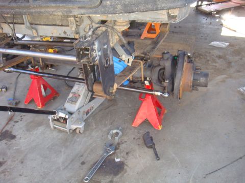 1992 Ford Bronco - Close-up of vehicle axle and suspension work in progress, with tools laid out on the concrete floor.