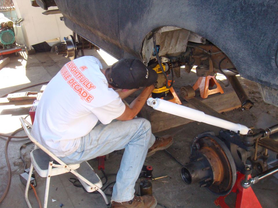 Man working on rear axle assembly of a vehicle, with suspension parts visible