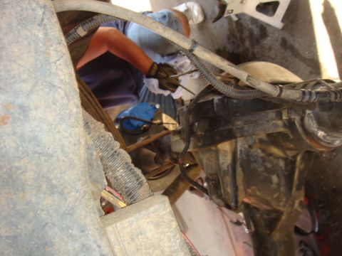 1992 Ford Bronco - Close-up of a mechanic's hands working on a vehicle's rear axle and suspension components.