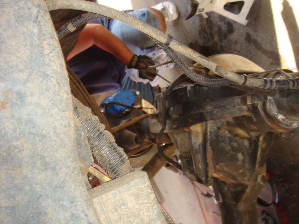 Mechanic wearing gloves works on a vehicle's rear axle assembly. Leaf springs and suspension components are visible