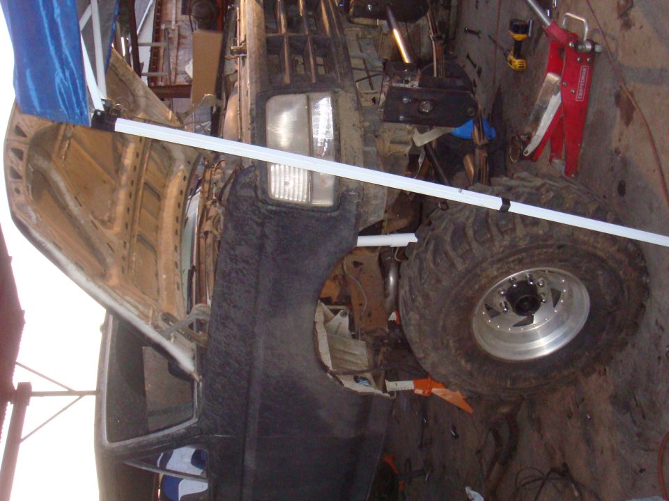 Off-road vehicle with large tires, possibly undergoing modifications. Hood is open, showing engine components