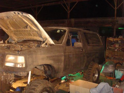 1992 Ford Bronco - A 1992 Ford Bronco is undergoing repairs in a dimly lit garage, with its hood raised.
