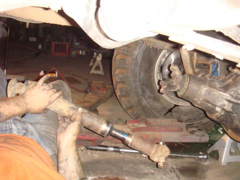 1992 Ford Bronco - Mechanic working on a driveshaft, with vehicle components like tire and axle in view.