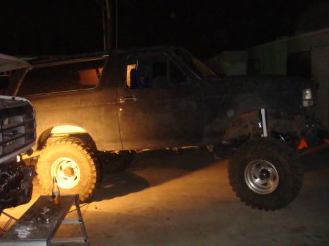 1992 Ford Bronco - A dark-colored Ford Bronco with lifted suspension and large tires is parked next to another vehicle.