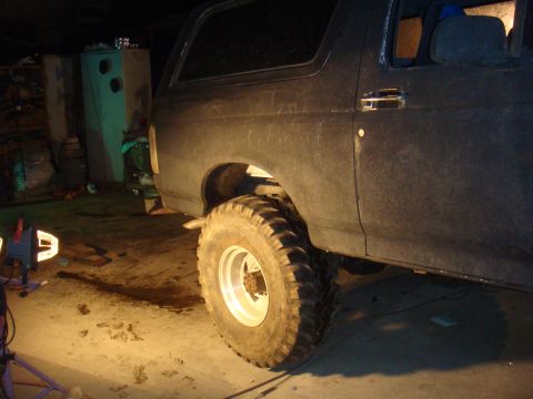 1992 Ford Bronco - A dark Ford Bronco is parked indoors, illuminated by artificial light, showing its large tires and side profile.