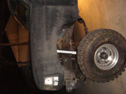 1992 Ford Bronco - The front quarter panel and wheel of a black 1992 Ford Bronco are visible, with the vehicle appearing to be in a garage or workshop.