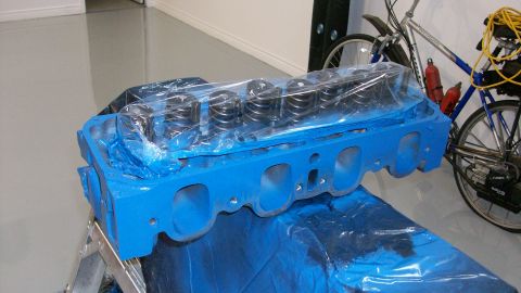 1973 Ford Ranchero - A blue engine cylinder head, likely for a Ford vehicle, is covered in plastic wrap and sits on a stand. A bicycle is visible in the backgro…