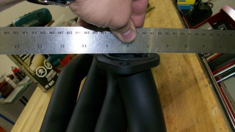 1973 Ford Ranchero - A ruler is used to measure a black exhaust manifold, likely for an engine part.