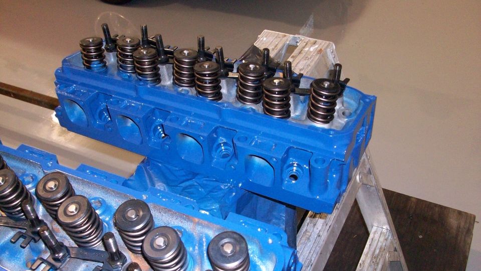 Blue-painted cylinder heads with valve springs on a metal stand in a shop